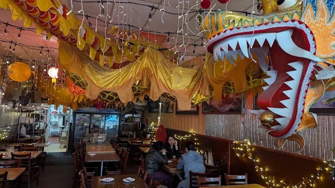 Close-up interior view of Mission Chinese Food in San Francisco focusing on the head of the large, colorful dragon decoration and a dense arrangement of string lights.