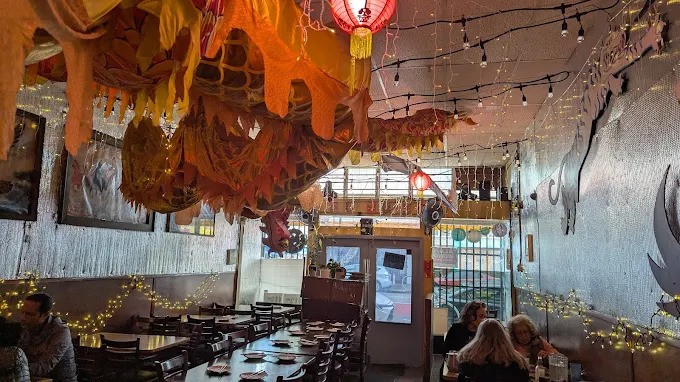 Detailed interior view of Mission Chinese Food in San Francisco showing a large section of the yellow dragon decoration, string lights, and simple wooden dining tables.