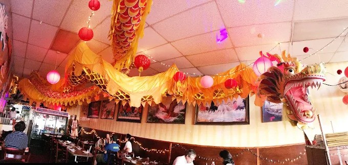Interior view of Mission Chinese Food in San Francisco, featuring a large, ornate yellow dragon decoration hanging from the ceiling, red lanterns, string lights, and patrons dining.