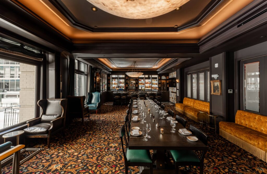 An elegant, dark wood-paneled private dining room with a long table set for a group, backed by a full bar. Features include plush velvet seating in mustard yellow and a large, ornate rug, perfect for a sophisticated Christmas in San Francisco gathering.