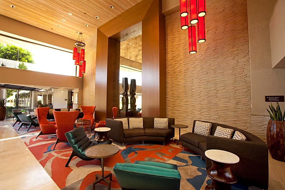 The vibrant and spacious lobby of the Hilton Palm Springs, showcasing mid-century modern furniture, colorful rugs, and tall red light fixtures, ready to welcome the Splash House 2026 crowds.