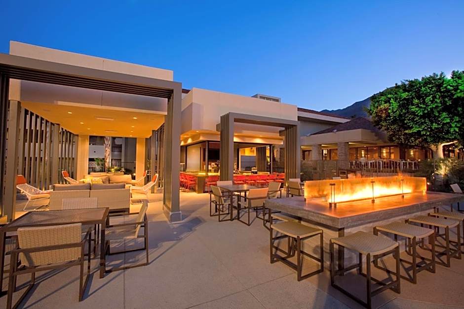 The modern outdoor patio at Hilton Palm Springs at dusk, featuring a long linear fire pit table and stylish seating areas where Splash House 2026 guests can lounge between pool parties.