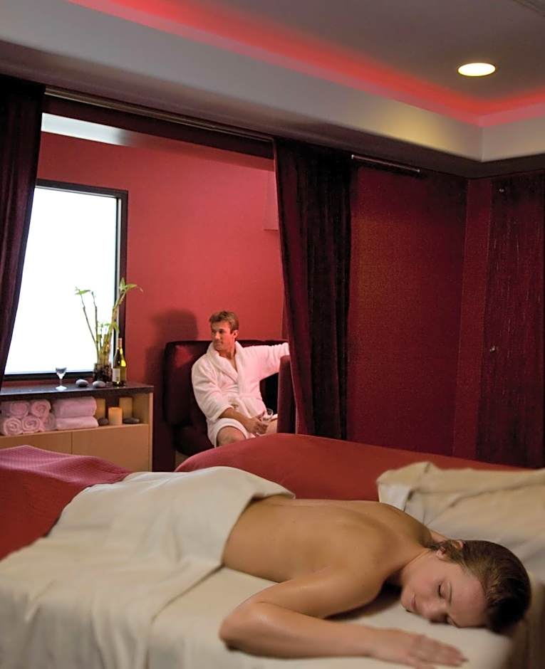 A serene indoor spa treatment room at the Hilton Palm Springs, featuring deep red walls and a couple enjoying a relaxing experience, perfect for recovery during the Splash House 2026 festival weekends.