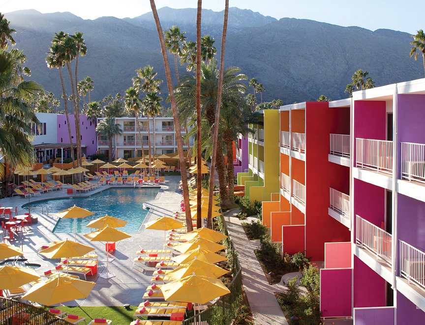 A close-up view of the multi-story hotel wings, where each balcony partition is painted a different bold color like pink, orange, yellow, and purple. In the foreground, neat rows of yellow patio umbrellas line the poolside.