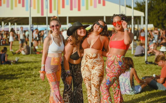 four women standing arm to arm while on the lawn at the Austin City Limits Music Festival 2025 wearing sexy bikini tops and sunglasses smiling and laughing