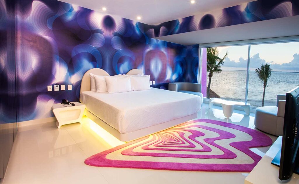 Modern bedroom design at Temptation Cancun Resort with colorful walls, illuminated bed, and oceanfront view in Cancun, Mexico.