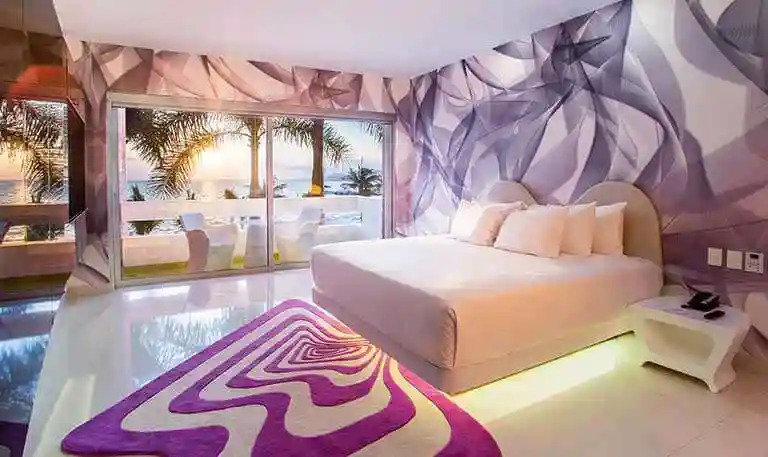 Trendy Temptation Cancun Resort room featuring vibrant wall art, king bed, and balcony overlooking the Caribbean Sea.