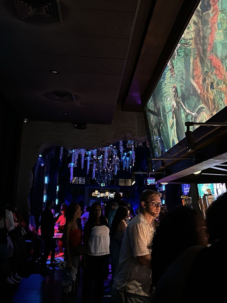 Crowded, dark interior of Dive Bar in Sacramento, known for its unique decor including dangling lights and a large artistic mural above the bar.