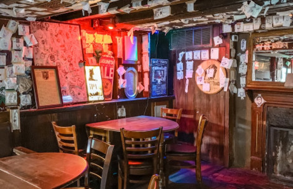 A cozy corner inside Abe’s on Lincoln in Savannah, featuring wood-paneled walls, a fireplace, and numerous drawings or notes tacked to the walls and ceiling.