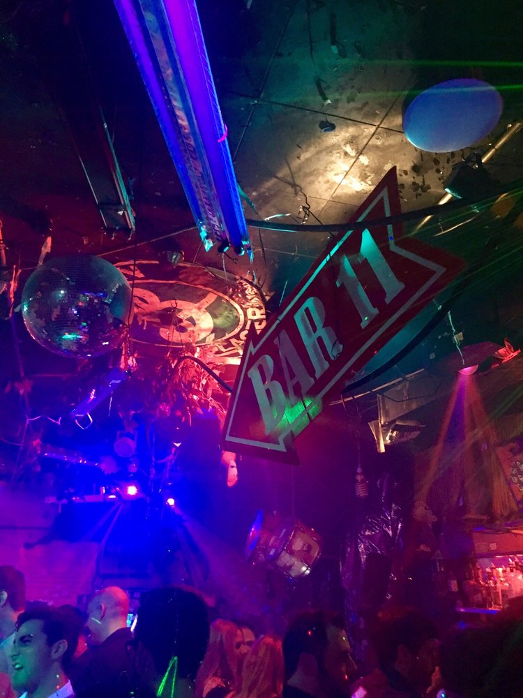 Interior of Bar 11 in Pittsburgh, a crowded, eclectically decorated dive bar with a disco ball, a large "BAR 11" arrow sign, and colorful party lights. This is one of the 'best dive bars near me' in Pittsburgh.