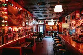 The dimly lit, narrow interior of Delux Café in Boston, showing red walls covered in framed photos, booths on one side, and a bar with stools on the other.