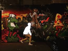 A person in a reflective jacket walks past a large, colorful graffiti mural inside the dimly lit Lone Wolf dive bar in Brooklyn.