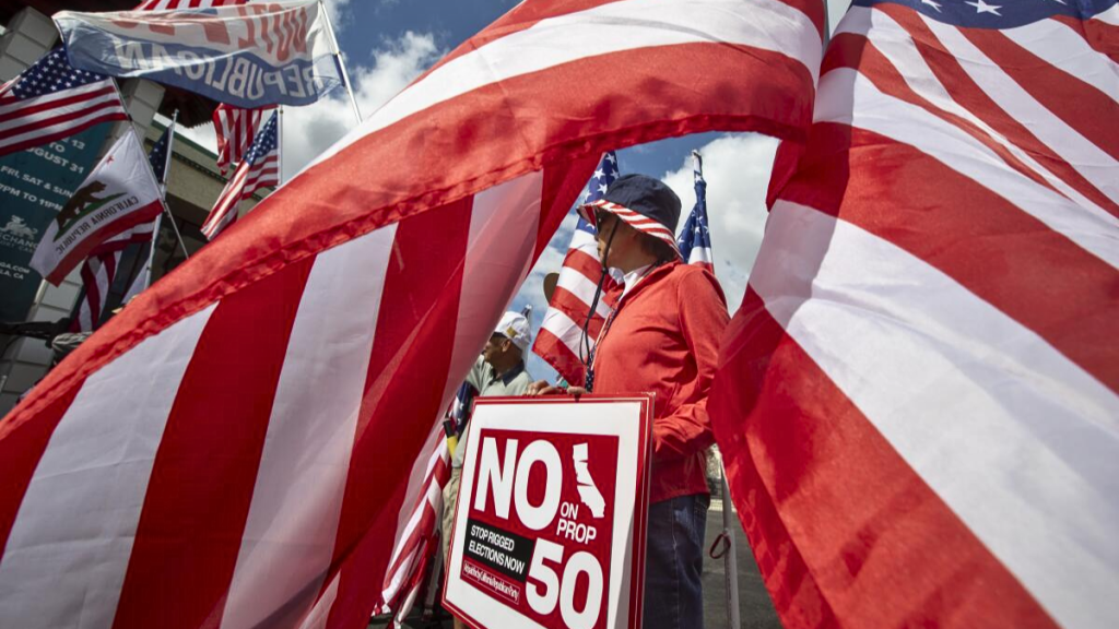 Rally attendees opposing Prop 50, waving American flags and holding signs to stop gerrymandering and political control in California