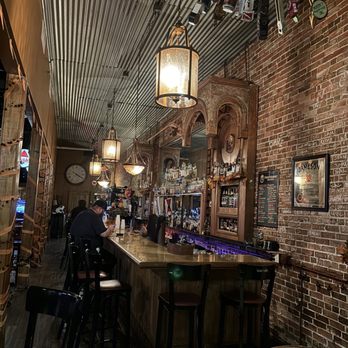 Interior of The Dirty Shame in Tampa, showing a long wooden bar, exposed brick walls, and ornate lighting fixtures. A must-visit when looking for the 'best dive bars near me' in Tampa.