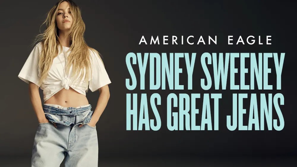 A promotional image for an American Eagle Sydney Sweeney jeans ad campaign. Actress Sydney Sweeney stands with her hands in the pockets of low-slung, light-wash jeans and a white cropped, knotted t-shirt, exposing her midriff. Bold white and blue text reads "AMERICAN EAGLE SYDNEY SWEENEY HAS GREAT JEANS."