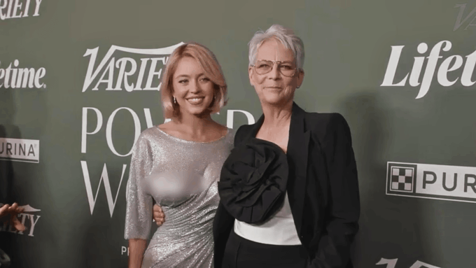 Sydney Sweeney and Jamie Lee Curtis posing together on a red carpet in front of a green and white background. Sydney Sweeney is smiling at the camera with her arm around Jamie Lee Curtis, who is also smiling softly at the camera.