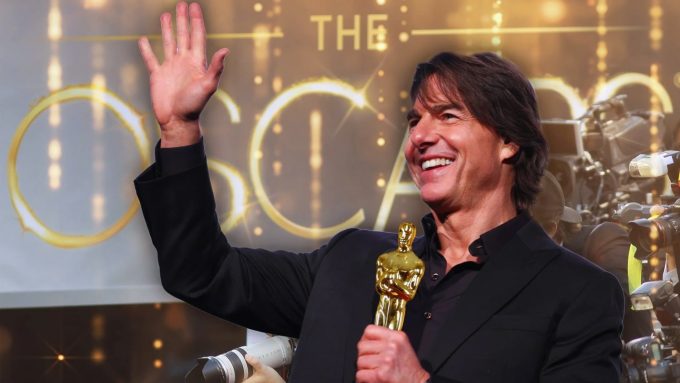 Tom Cruise smiling, waving, and holding an Oscar statuette amidst a crowd of photographers.