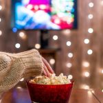 a hand on popcorn depicting Top 10 Christmas movies on Netflix poster image, promoting the best holiday movies on Netflix for 2025.
