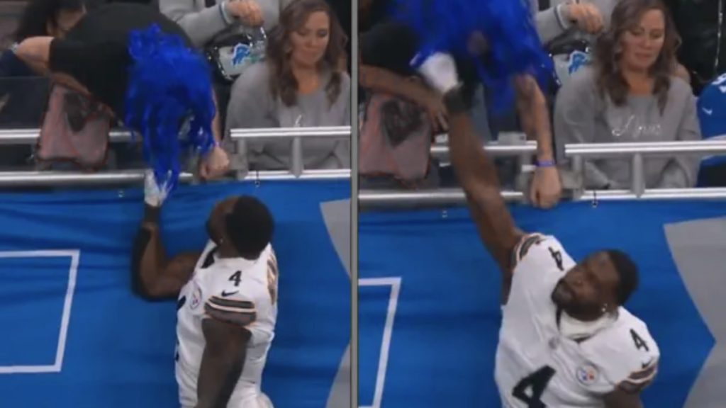A captured video still from the CBS broadcast showing DK Metcalf's arm extended toward a fan at Ford Field. The fan is seen leaning over the railing while Metcalf appears to make contact with his hand near the fan's face or jersey.