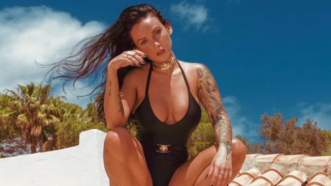 Fashion influencer Kayla Lauren posing in a sleek black belted swimsuit and gold jewelry on a Mediterranean-style rooftop, showcasing 2026 summer style trends and tattoo artistry.
