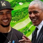 A composite digital graphic featuring Los Angeles Dodgers player Mookie Betts and former President Barack Obama. Betts is on the left wearing a black "LA" baseball cap and a black t-shirt, while Obama is on the right in a white dress shirt and dark patterned tie. Both men are smiling broadly. The background is a bright, saturated aerial view of a lush green golf course with winding fairways and sand traps.