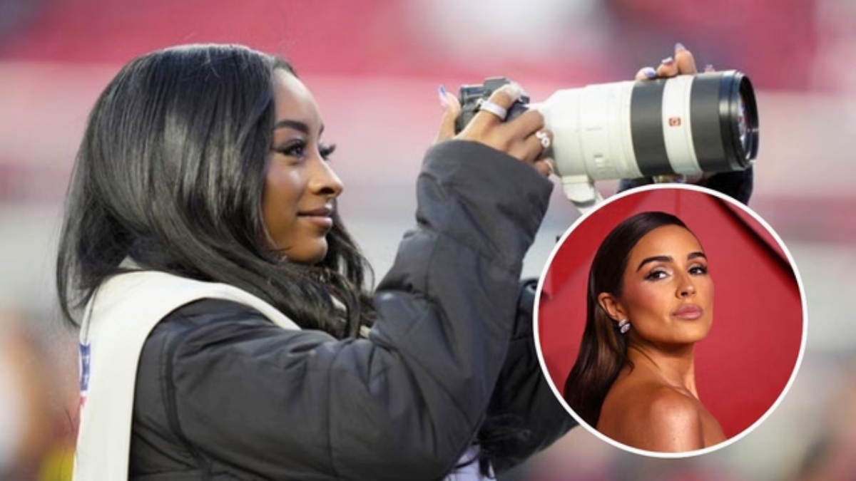 Olympic gymnast Simone Biles smiles while looking through a professional Sony telephoto camera lens on the sidelines of Levi's Stadium. She is wearing a black puffer jacket and a white NFL media vest. An inset circle shows a glamorous portrait of Olivia Culpo.
