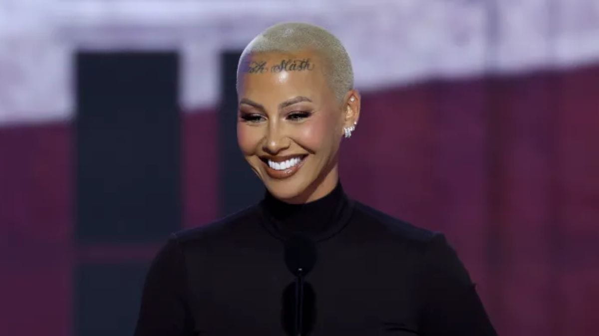 Model and activist Amber Rose smiling on stage with her signature buzz cut and forehead tattoo during a public event.
