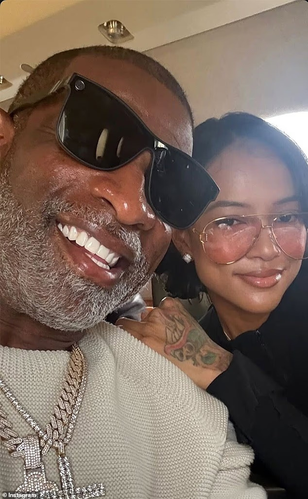 A close-up selfie of Deion Sanders and Karrueche Tran smiling together. Deion is in the foreground wearing large black sunglasses and a diamond-encrusted chain, while Karrueche leans in next to him wearing aviator-style glasses.