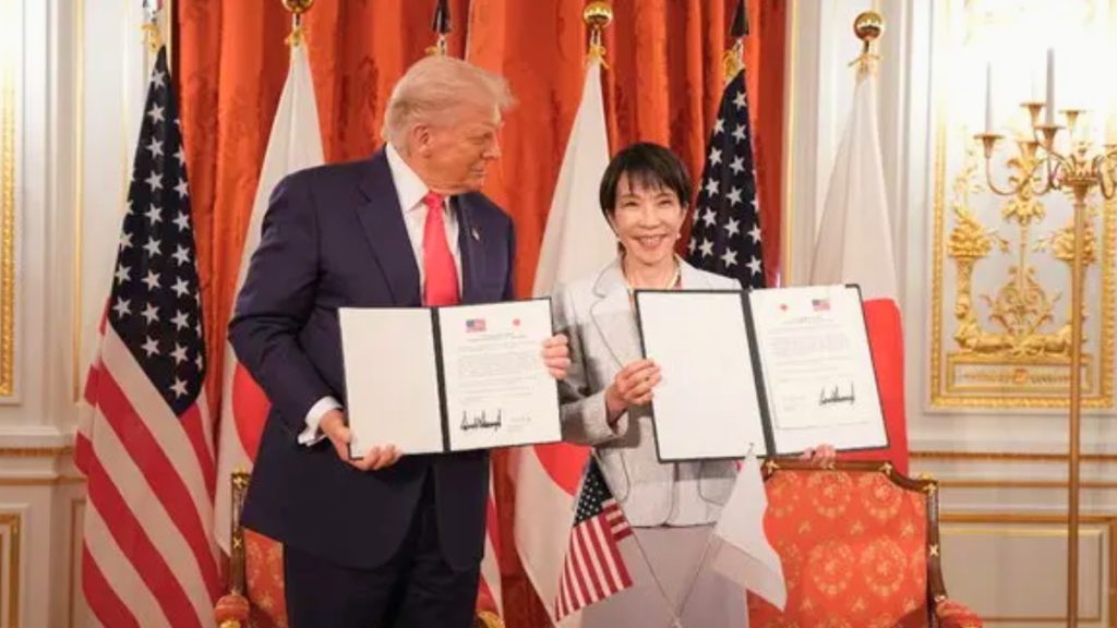 A close-up of President Trump and Prime Minister Takaichi shaking hands in front of a row of American and Japanese flags. This historic meeting solidified a $36 Billion US Investment focused on energy and critical minerals projects in Ohio, Texas, and Georgia.