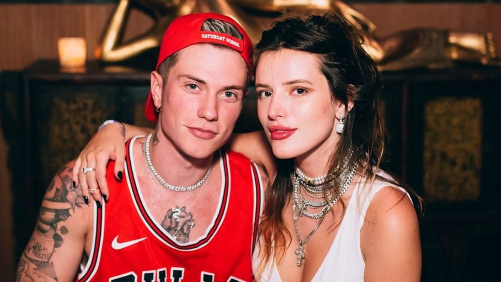 Bella Thorne Valentine’s Day memories featuring the star and Benjamin Mascolo; Bella wears a white top and layered silver chains while Benjamin wears a red Chicago Bulls jersey and a backwards red cap.