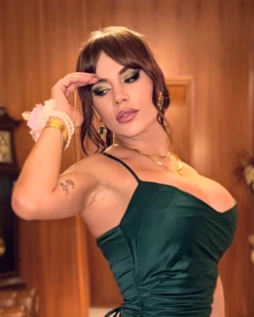 Carolina Cazadora in a dark green satin dress with elegant makeup and gold jewelry.