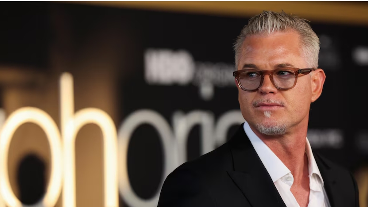 A professional headshot of actor Eric Dane at a red carpet event. He is wearing a black suit jacket over an unbuttoned white shirt and amber-tinted glasses. The background is blurred with a glowing "Euphoria" sign visible. Overlaying the image is a fake news headline claiming he passed away at age 53 after a battle with ALS.