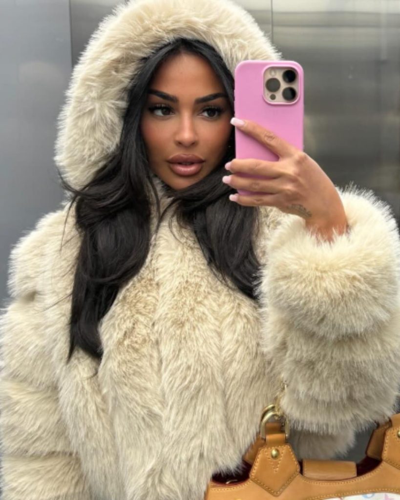 German Onlyfans Influencer Mary Crib taking a miror selfie wearing a cream colored, hooded fur coat.