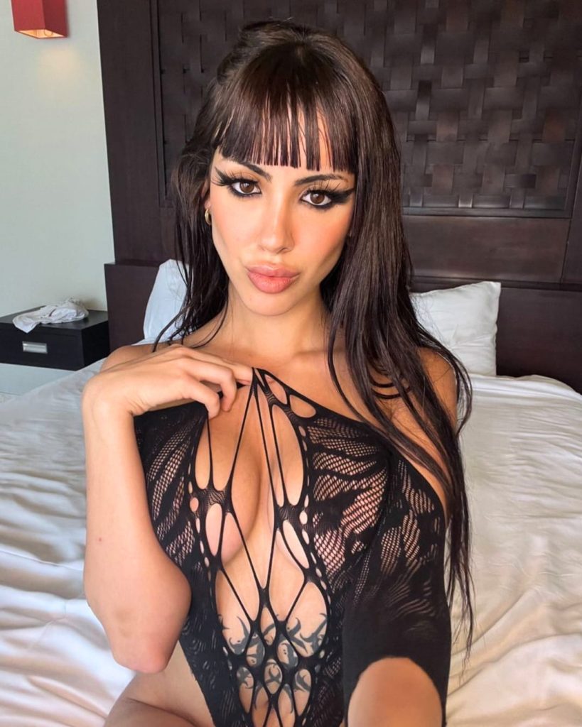 Jasmine Llamas wearing black lace bodysuit, Spain OnlyFans model posing in bedroom setting.
