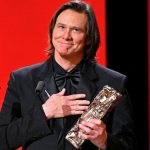 Jim Carrey holds a César Award trophy to his chest with an emotional expression during his acceptance speech.