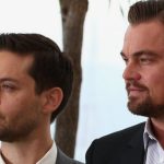 Actors Leonardo DiCaprio and Tobey Maguire looking toward the side during a Super Bowl party; DiCaprio is sporting a beard and Maguire is in a white dress shirt.