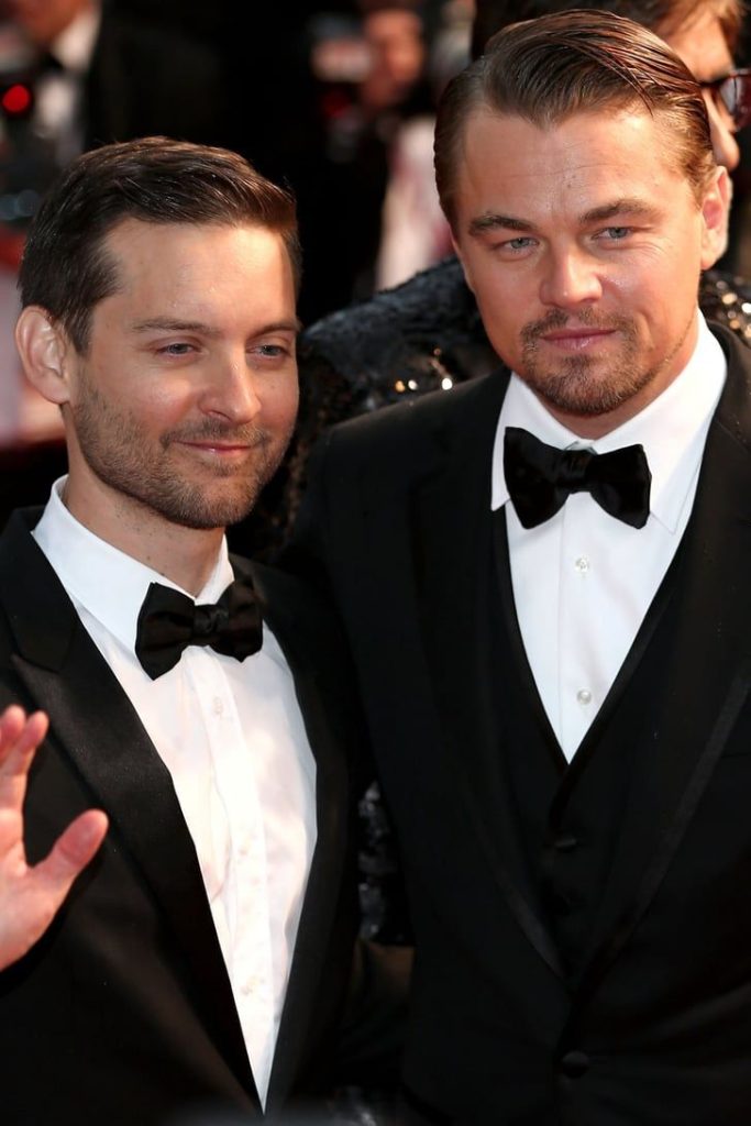 Longtime friends Leonardo DiCaprio and Tobey Maguire wearing formal black tuxedos and bow ties while attending a high-profile Super Bowl event.