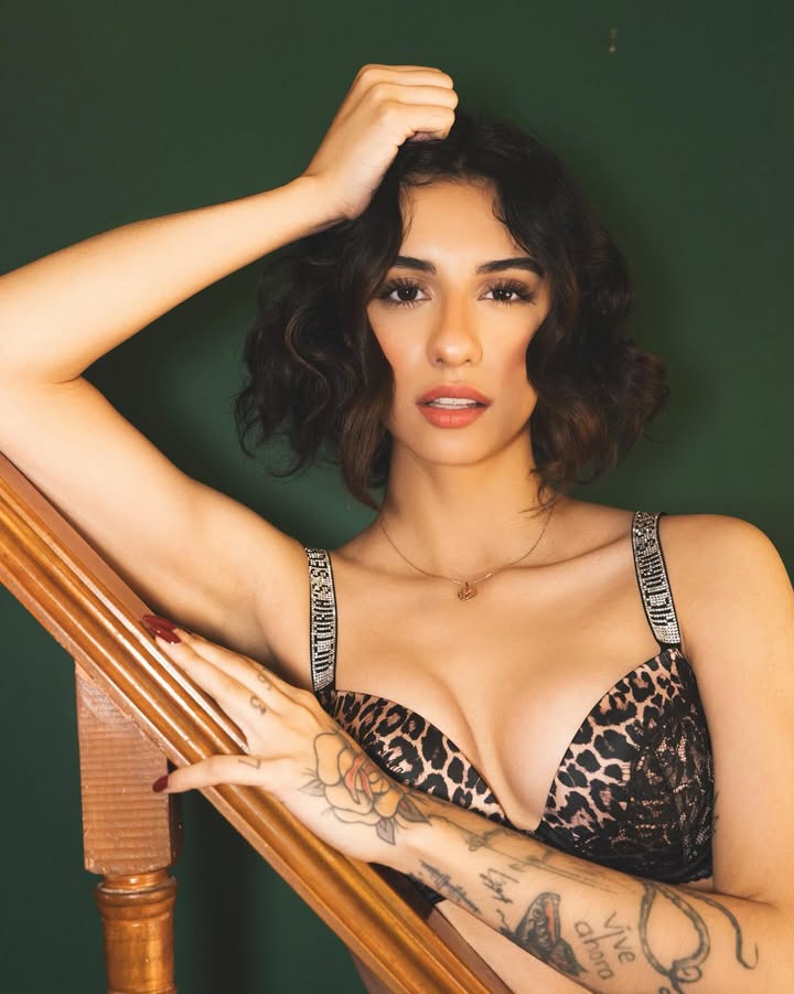 A Mexican model with short wavy dark hair posing on a wooden staircase in a leopard print bra.