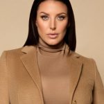 Portrait of Australian influencer Angela White wearing a tan turtleneck and matching wool blazer against a neutral beige background.