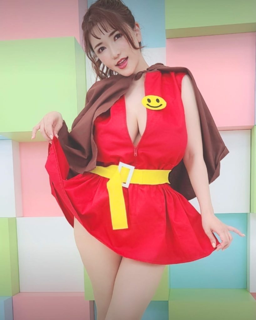Japanese cosplay model, Anri Okita wearing red dress with yellow belt and cape posing in colorful studio background.