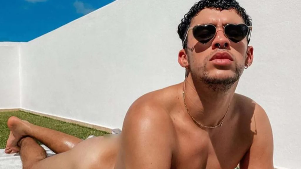 Bad Bunny birthday sunbathing photo of Benito wearing heart-shaped sunglasses while lounging outside on a white terrace.