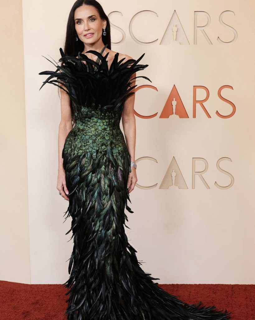 Demi Moore wearing a dramatic strapless emerald green and black feathered Gucci gown on the Oscars Red Carpet 2026.