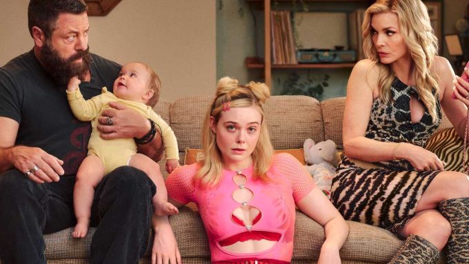 Elle Fanning sits on a couch wearing a pink mesh top, flanked by a bearded man holding a baby and a woman in a leopard-print dress, in a scene from Margo's Got Money Troubles.