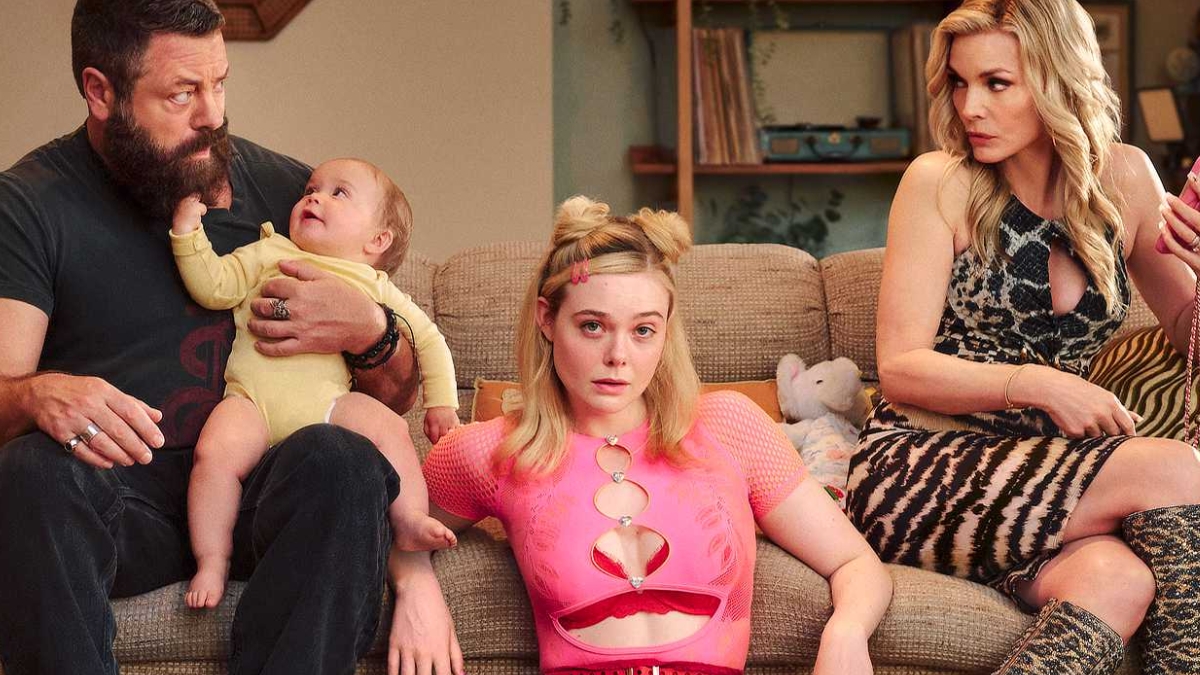 Elle Fanning sits on a couch wearing a pink mesh top, flanked by a bearded man holding a baby and a woman in a leopard-print dress, in a scene from Margo's Got Money Troubles.