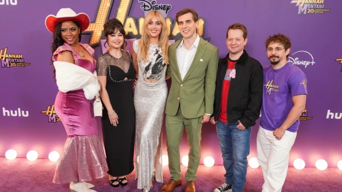 A full-length photo of a group of six posing against a purple wall at the Hannah Montana Reunion event.