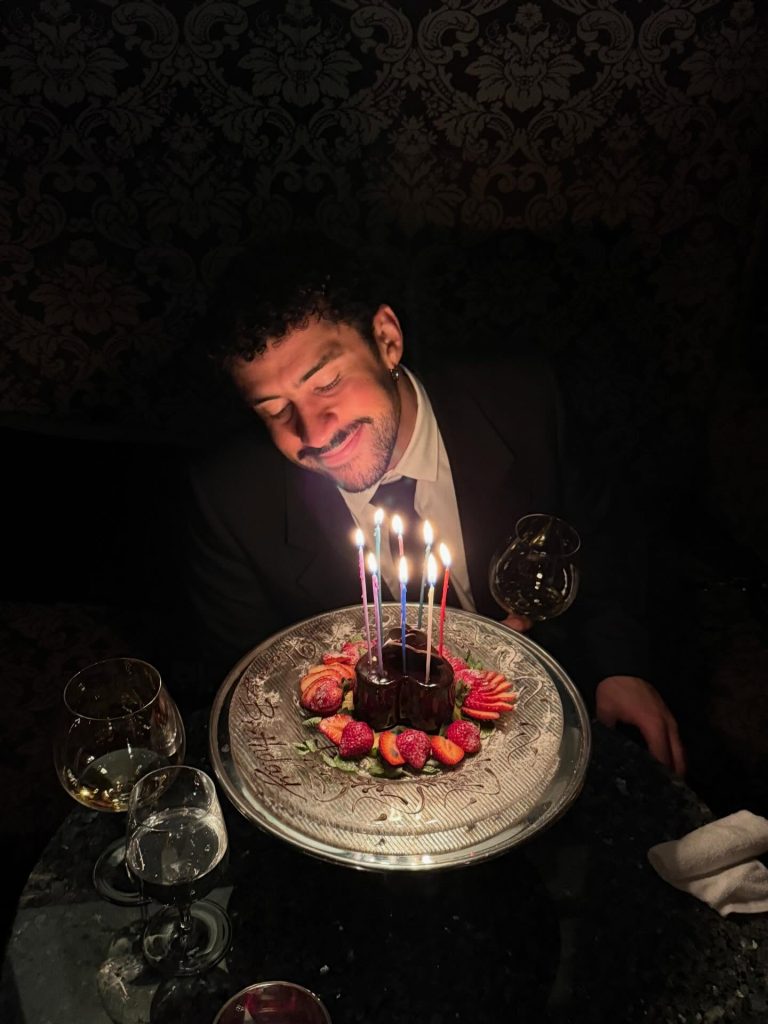 Bad Bunny birthday moment showing Benito smiling over a chocolate heart-shaped cake with lit candles and strawberries.