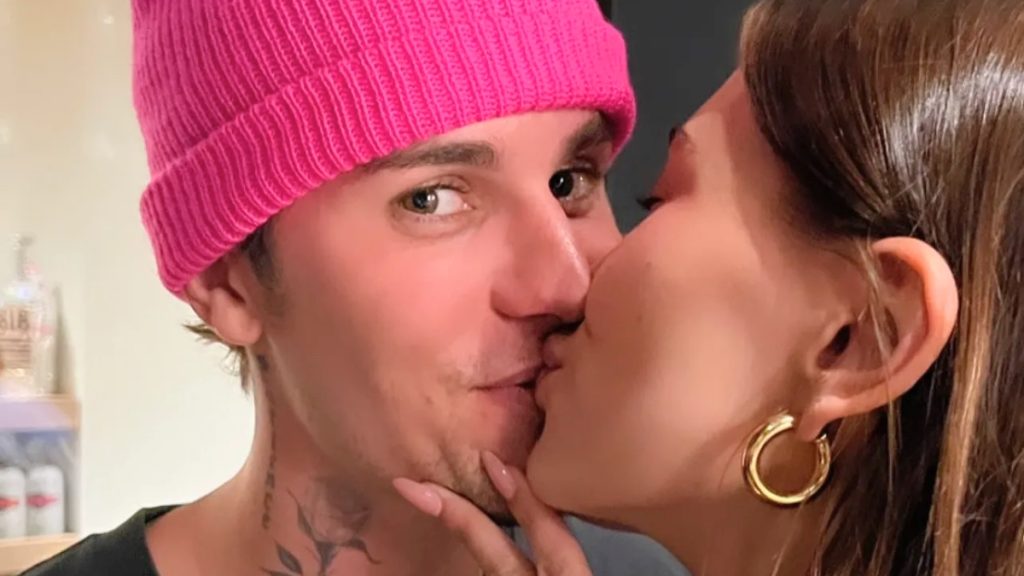 A close-up of Hailey Bieber kissing Justin on the cheek as he wears a bright pink beanie during his Justin Bieber Birthday festivities.