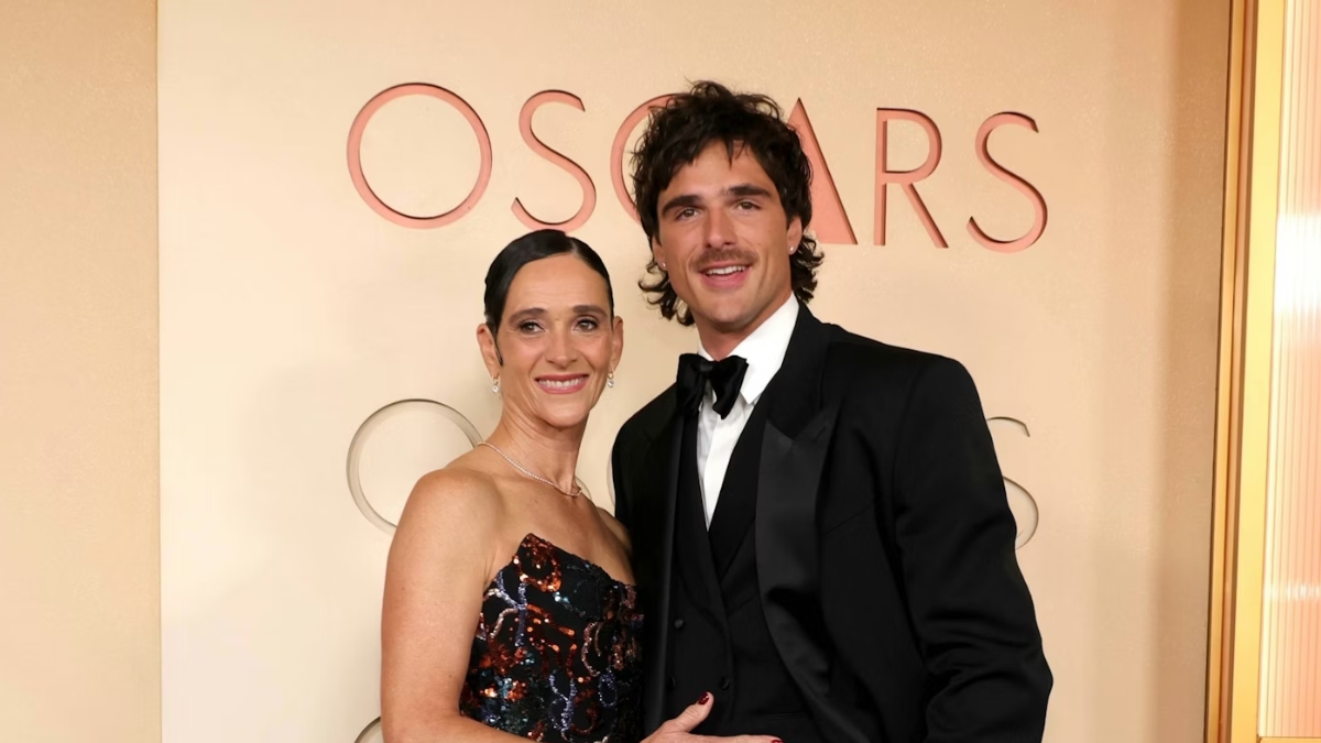 A heartwarming portrait of Jacob Elordi and his mother, Melissa, on the Oscars red carpet. Jacob wears a sleek tuxedo, and Melissa is in a sequined gown, both beaming for the cameras.