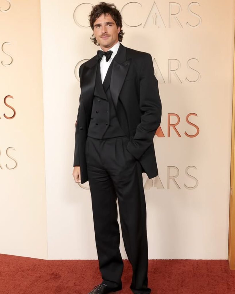 Jacob Elordi posing  in a vintage-inspired oversized black tuxedo jacket and wide-leg trousers.