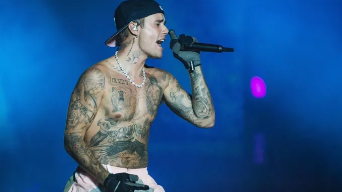 A shirtless, tattooed Justin Bieber performing on stage with a microphone, capturing the "Love Over Fame" theme of the Justin Bieber Birthday.